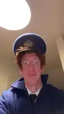A man dressed in a full blue postman uniform, complete with hat and satchel, performs an energetic dance routine in a room. He smiles and moves rhythmically to upbeat music, creating a cheerful and entertaining short clip. by @uk-gos with Original Sound by uk-gos