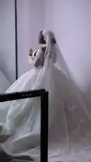 A stunning bride showcases her breathtaking white lace wedding gown with a long veil and matching gloves. She poses gracefully in a modern studio setting, highlighting the intricate details of her dress. The groom, dressed in traditional white attire, joins her for intimate moments and formal portraits, creating a romantic and culturally rich atmosphere. by @miji-bello with Original Sound by miji-bello