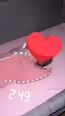 A baby peacefully sleeping in a pink swaddle blanket inside a crib. The scene is calm and serene, with soft lighting and a digital clock showing 2:49 in the background. A large red heart emoji is overlaid on the image, adding a touch of affection and warmth to the moment. by @framesofbrum with Original Sound by framesofbrum