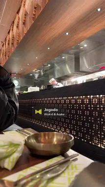 This behind-the-scenes look offers a real-time view of a bustling restaurant kitchen. From the perspective of a diner at the counter, you can see chefs actively preparing meals in a modern, open-plan setting. Staff move efficiently through the space, highlighting the dynamic and collaborative environment of a professional culinary team. by @djspinall with Jogodo by Wizkid & Asake