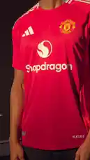 A Manchester United football player showcases the team's new red jersey with the Snapdragon sponsor logo during a professional photoshoot. The athlete poses confidently against a large backdrop of a bridge, highlighting the shirt's design details. by @manutd with original sound