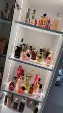 A curated display of a personal perfume collection, showcasing a variety of luxury fragrance bottles arranged neatly on illuminated shelves. The scene highlights the artistry of the bottles, their colors, and shapes, creating a visually appealing and aspirational aesthetic. by @priscy2450 with Soft girl era by Yunna Serene