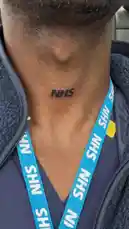 A close-up shot focuses on a person's neck, showcasing a permanent 'NHS' tattoo. They are wearing a blue NHS lanyard over dark scrubs, clearly identifying them as a member of the UK's National Health Service. The background suggests they are inside a vehicle. by @uk-gos with Original Sound by uk-gos