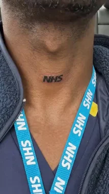 A close-up shot focuses on a person's neck, showcasing a permanent 'NHS' tattoo. They are wearing a blue NHS lanyard over dark scrubs, clearly identifying them as a member of the UK's National Health Service. The background suggests they are inside a vehicle. by @uk-gos with Original Sound by uk-gos