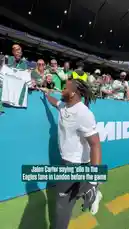 Philadelphia Eagles player Jalen Carter is seen walking along the sideline before a game in London, waving and saying 'ello' to fans in the stands. He is wearing a white t-shirt and black pants, interacting with supporters who are dressed in team colors. by @eagles with Original Sound by eagles