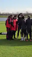 This video captures a Manchester United training session on a sunny day. Players, some wearing red training bibs over their black kits, gather in a huddle before dispersing across the grass field to begin drills. Coaches and staff are visible, overseeing the session. The atmosphere is focused and professional, showcasing the behind-the-scenes preparation of a top-tier football club. by @manutd with Original Sound by manutd