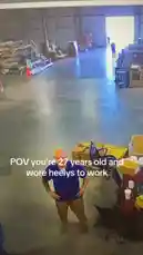 A man in a warehouse stands with his hands on his hips as another person runs past him wearing Heelys roller shoes. The text overlay reads 'POV you're 27 years old and wore heelys to work'. The scene captures a lighthearted moment in a workplace setting. by @uk-gos with Original Sound by uk-gos