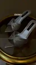 A close-up shot showcases a pair of elegant silver, pointed-toe mule heels from the brand DIANA. The shoes feature a glittery bow detail across the vamp and are displayed on a reflective, gold-rimmed surface. Text overlay humorously states, 'money can't buy happiness but it can buy you a pair of Heels,' setting a lighthearted tone. by @bydiana.co with Original Sound by Contains: Bliss - Klsr