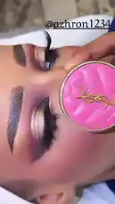 A close-up shot captures a person showcasing their finished glamorous makeup look, focusing on bold, defined eyebrows and dramatic eyes with shimmery bronze and gold eyeshadow. A hand holds a distinctive bright pink quilted compact mirror with a gold YSL logo, adding a touch of luxury to the beauty routine. by @azhron1234 with original sound