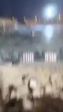 A white pickup truck performs high-speed drifting maneuvers on a large dirt track at night. The vehicle creates dramatic clouds of dust and smoke as it executes tight turns and burnouts under powerful stadium lights. Spectators can be seen watching from elevated bleachers in the background. by @zf_v81 with Original Sound by zf_v81