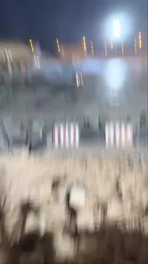 A white pickup truck performs high-speed drifting maneuvers on a large dirt track at night. The vehicle creates dramatic clouds of dust and smoke as it executes tight turns and burnouts under powerful stadium lights. Spectators can be seen watching from elevated bleachers in the background. by @zf_v81 with Original Sound by zf_v81