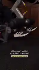 This close-up video showcases a person using a leg press machine, focusing on their feet in black Adidas sneakers as they push against the footplate. The gym setting features dark flooring and wooden walls. On-screen Arabic text reads 'اشتريكي، وابدئي رحلتك' ('Buy it, start your journey') and 'YOUR SPOT IS WAITING', with a call to action below for 'العروض و الفواصل القواصيل معانا' ('Deals and breaks with us'). The Active Circle brand is highlighted through the equipment and promotional message. by @activecircle with original sound