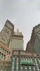 This video offers a stunning upward view of the iconic Abraj Al-Bait Clock Tower in Mecca, Saudi Arabia. The camera remains static, focusing on the grandeur of the tower and its surrounding buildings against a cloudy sky. Arabic text overlays the scene, displaying Islamic phrases such as 'إِنَّ اللَّهَ وَمَلَائِكَتَهُ يُصَلُّونَ عَلَى النَّبِيِّ' (Indeed, Allah and His angels send blessings upon the Prophet) and 'يَا أَيُّهَا الَّذِينَ آمَنُوا صَلُّوا عَلَيْهِ وَسَلِّمُوا تَسْلِيمًا' (O you who have believed, send your prayers upon him and greet him with peace). The overall atmosphere is one of reverence and awe, capturing the architectural beauty of one of the world's most famous landmarks. by @s3432x with Original Sound by s3432x