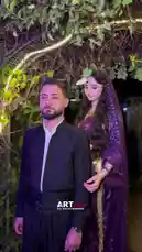 A beautifully lit outdoor scene captures a couple sharing an intimate embrace. The woman, adorned in a stunning purple sequined outfit and veil, wraps her arms around the man in a black traditional tunic. Set against a backdrop of lush greenery illuminated by golden string lights, their affectionate moment creates a romantic and cinematic atmosphere. by @artvideo.me with artvideo.me by Original Sound