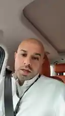 In this candid behind-the-scenes clip, Bader Alodah is seen inside a luxury vehicle, speaking directly to the camera. He wears a white collared shirt and a black lanyard, occasionally gesturing as he shares his thoughts. The modern car interior features tan leather seats and a panoramic sunroof, suggesting a relaxed yet professional setting. This personal vlog-style moment offers viewers an intimate look into his daily life and communication style. by @guruofmarketing with Original Sound by guruofmarketing