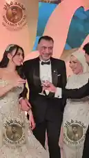 This video captures a joyful moment at a wedding reception. A bride in a stunning silver gown stands with her father, who is dressed in a tuxedo. They are joined by another man in a tuxedo, and they all share a warm, celebratory interaction. The background features elegant decorations and soft lighting, creating a festive atmosphere. by @mo.fouadziko with Original Sound by mo.fouadziko