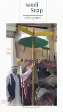 This short clip from 'Saudi Snap' features a man in traditional Saudi attire demonstrating a unique, hand-cranked windmill-like device. He turns a central pole, causing colorful blades to rotate rapidly, showcasing a piece of local heritage or a functional mechanism. The setting appears to be a workshop or home, filled with textiles and equipment. by @saudi-snap2025 with Original Sound by saudi-snap2025