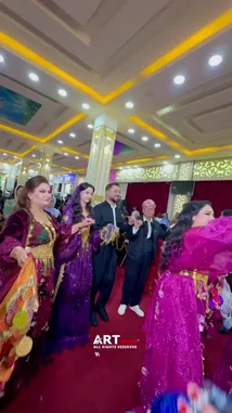 Witness a vibrant traditional dance performance featuring women in ornate purple and magenta costumes adorned with gold accessories. Dancers gracefully move across a red carpeted hall with decorative pillars and red curtains, surrounded by guests in formal attire, including men in black suits and traditional headwear. The festive atmosphere suggests a wedding or cultural event, showcasing heritage through synchronized choreography and elaborate folk costumes. by @artvideo.me with artvideo.me by Original Sound