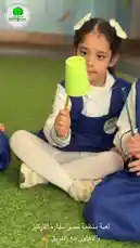 Children in blue school uniforms sit on green artificial turf, proudly displaying their handmade crafts. Each student holds a bright green cup attached to a stick, creating a simple yet creative representation of an eco-friendly theme. The atmosphere is joyful and educational, capturing a moment of hands-on learning and celebration. by @ajyalf with Original Sound by ajyalf
