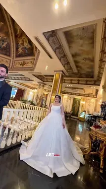 A bride in a stunning white gown and tiara walks arm-in-arm with her groom in a luxurious palace hall. They pose together, sharing an intimate moment before she turns to admire the ornate surroundings. The opulent setting features golden pillars and a magnificent ceiling fresco, creating a romantic and grand atmosphere. by @artvideo.me with artvideo.me by Original Sound