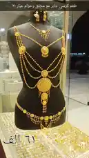 A stunning display of elaborate golden bridal jewelry set against a black mannequin. The intricate pieces, including a multi-layered necklace, matching earrings, and a decorative waist chain, showcase exquisite craftsmanship. The camera slowly pans around the display, highlighting the shimmering details in a well-lit retail setting. by @hussain.2022a with original sound