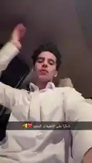 A young man, identified as Inam Sultan, films himself in selfie mode while sitting in the driver's seat of a car at night. He wears a white button-down shirt and makes various hand gestures towards the camera, including pointing and making an 'OK' sign. The interior of the car is dimly lit, creating an intimate vlog-like atmosphere. by @by.sul with Snapchatter by Original Sound