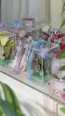 A stylish presentation of beautifully crafted gift boxes by Joy Narcissus. The video showcases transparent acrylic containers filled with glitter, personalized Arabic calligraphy, fresh flowers, and small accessories like perfume bottles and makeup brushes. A woman in a floral dress unboxes several items, revealing their contents and highlighting the intricate details and luxurious design of each piece. This elegant display is perfect for anyone looking for creative gifting ideas. by @joy.narcissus with Original Sound by Contains: عيد إثراء - Zena Emad زينه عماد