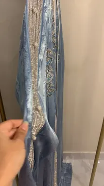 A close-up showcase of a stunning light blue abaya with intricate silver embroidery, displayed on a mannequin. The camera pans out to reveal the full garment, highlighting its elegant design and craftsmanship. by @needle_t with needle_t by Original Sound