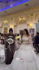 A stunning wedding party unfolds in a grand, opulent hall. The bride, radiant in a sparkling white gown, walks gracefully alongside her mother-in-law, who wears a chic black sequined dress. They are joined by other guests, including bridesmaids in coordinated blue and green gowns, and adorable flower girls in charming white dresses. The atmosphere is celebratory and sophisticated, with everyone smiling and enjoying the special occasion. by @artvideo.me with artvideo.me by Original Sound