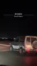A white off-road SUV with a spare tire mounted on the rear door drives along a desert highway at night. The vehicle's taillights are illuminated, and its license plate is visible. The surrounding area is dark, with distant lights on the horizon, suggesting a remote location. The perspective is from another vehicle following behind, capturing the journey under the cover of darkness. by @azozi.5562 with original sound