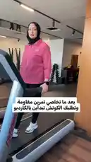 A woman wearing a pink jacket and black hijab is exercising on a Life Fitness treadmill inside a modern gym. She stands on the machine, looks at the camera, speaks, gestures with her hands, and raises her arms in celebration before stepping off. The Arabic text overlay translates to 'What workout do you recommend for me? And what do you think about cardio?'. The setting appears to be a fitness center named Active Circle. by @activecircle with Original Sound by activecircle