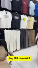 A man browses through a new collection of casual wear at a retail store in Al Jubail Al Sharqiyah. He points out various t-shirts and pants on display, highlighting their designs and prices. A voiceover confirms the items are brand new and discusses pricing details. by @dalilnet with Original Sound by dalilnet