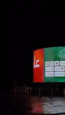 Experience a cinematic night drive through Riyadh, Saudi Arabia. The journey begins with a close-up of a massive, curved digital billboard displaying 'نجمة' and 'صحة' in Arabic, promoting Najd Health City. As the camera moves, it reveals a wider view of the wet, reflective road, illuminated streetlights, and a prominent red-and-white chevron sign guiding drivers along the curve. This atmospheric clip captures the modern urban landscape of Riyadh after dark. by @karim.alsaleh with مالك ديار تشابه قلب حايل ♥️ by 📍Hai’l