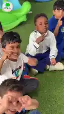 A joyful scene from مدارس أجيال الفيصلية الأهلية shows young students in their blue and white uniforms having fun on artificial turf. They make playful hand gestures for the camera before receiving ice cream bars as treats. The children are seen happily walking around, sharing snacks, and enjoying a special treat day together. by @ajyalf with Original Sound by ajyalf