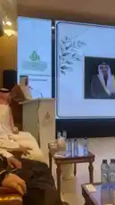 This video captures a formal event hosted by the 'Saudia Arabia's First Lady Foundation,' where speaker Yaser Al-Khamsan addresses an audience from a podium. The setting is a grand hall adorned with traditional decor, featuring guests in thobes and ghutras. A large screen displays Arabic text and a portrait of a prominent figure, likely the foundation's namesake. by @y_alkhmsan with Original Sound by y_alkhmsan