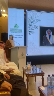 This video captures a formal event hosted by the 'Saudia Arabia's First Lady Foundation,' where speaker Yaser Al-Khamsan addresses an audience from a podium. The setting is a grand hall adorned with traditional decor, featuring guests in thobes and ghutras. A large screen displays Arabic text and a portrait of a prominent figure, likely the foundation's namesake. by @y_alkhmsan with Original Sound by y_alkhmsan