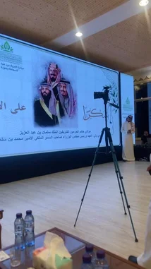 The video captures a formal event hosted by the Abdullah Rasool Al-Rasool Private Foundation For His Family in Riyadh. A man, identified as Yaser Al-Khamsan, delivers a speech at a podium in front of a large screen displaying Arabic text and images of Saudi royalty. The setting is a well-lit conference hall, and the speaker is dressed in traditional Saudi attire. by @y_alkhmsan with Original Sound by y_alkhmsan