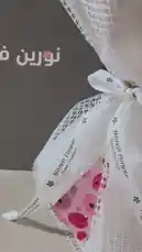 A close-up showcase of a stunning flower bouquet from Noren Flower boutique, tied with elegant white mesh and ribbon. The camera pans across the arrangement of pink roses and a single gerbera daisy before revealing a heartfelt Arabic message card inside, making it a perfect gift reveal. by @i_vcil with original sound