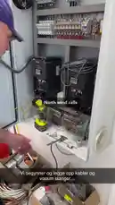 A craftsman from Viking Custom Craft works on an industrial electrical control panel, installing inverters and organizing wiring. He then moves to another area to run conduit and pull new cables through walls, demonstrating professional electrical installation techniques. by @vikingcustom with original sound