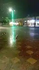 A dramatic nighttime scene unfolds as a heavy hailstorm blankets a city street, turning pavement into a reflective, icy surface. Vehicles cautiously drive through the downpour under bright streetlights, their headlights cutting through the dark sky filled with falling ice. Palm trees sway in the wind, and storefronts line the background, capturing the chaos and intensity of severe weather in an urban setting. by @fixedstructure with Original Sound by fixedstructure