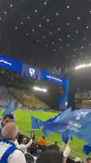 Experience the electric atmosphere inside a modern football stadium as Al Hilal fans passionately wave blue flags and chant in unison. The sea of supporters, dressed in team colors, creates a powerful visual spectacle under the bright lights, showcasing the intense passion of Saudi Arabian football culture. by @abood114 with Original Sound by abood114