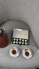 A stylishly arranged coffee setup featuring a modern armchair, ornate brass side tables, and a luxurious tea service. The scene includes a red thermos, heart-shaped chocolates, and decorative bottles, creating a cozy and sophisticated atmosphere perfect for relaxation. by @bee.8907 with Original Sound by bee.8907