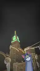 This captivating night-time video features the iconic cartoon character Tom from 'Tom and Jerry' superimposed onto real-world footage of Mecca, Saudi Arabia. The journey begins with a view of the illuminated Abraj Al Bait Clock Tower, then transitions to a ground-level perspective inside a building, showing Arabic signage for the 'Ministry of Islamic Affairs, Dawah, and Guidance' and the 'Makkah Chamber of Commerce'. The blend of animation and reality creates a surreal and intriguing travel experience. by @om-5p with Original Sound by om-5p