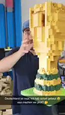 In this behind-the-scenes look, BigBang Bash proudly displays his enormous, partially completed LEGO World Cup trophy. He explains the project's origin—printing it in 3D—and shares the humorous story of how Germany's soccer match result determined how much of the model was built before the team was eliminated. Now, the massive LEGO creation sits incomplete, and he turns to his audience for help, asking them to comment with ideas on how to finish it. by @bigbangbash_off with Original Sound by bigbangbash_off