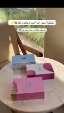 This stylish video showcases a curated collection of beauty and grooming products from the brand SOINS. It begins with three colorful 'Sweet Ice Candy' boxes, then transitions to a close-up display of perfumes, lip glosses, and nail polish. Arabic text overlays provide details about the items, including price ranges and descriptions like 'Sensuality,' 'Happiness,' and 'Glamour.' The elegant presentation on a marble table with a frangipani flower suggests a personal review or a showcase of a favorite set. by @soins_sa with Original Sound by soins_sa