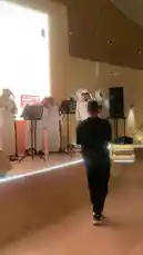 This video captures a live performance by a group of men in traditional Emirati attire, including dishdashas and ghutras, on a well-lit stage. A large screen behind them displays Arabic text and a car illustration, suggesting a formal event like a national celebration or cultural showcase. The atmosphere is celebratory, with audience applause and cheers audible throughout. A cameraman films the event, emphasizing its significance. The setting and presentation style point to a professionally organized gathering focused on Emirati heritage. by @y_alkhmsan with Original Sound by y_alkhmsan