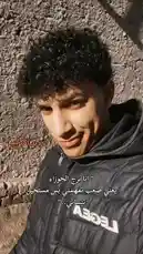 This short-form video features the creator, سُوفــــــا Wildcats, against a rustic stone wall. He wears a black puffer jacket with 'LEGEA' branding, looking directly into the camera with a subtle smile. Arabic text overlays his image, conveying a personal message about self-acceptance and resilience. The bright sunlight creates strong shadows, highlighting his curly hair and determined expression, suggesting a narrative of overcoming challenges. by @sofaa_66 with sofaa_66 by Original Sound