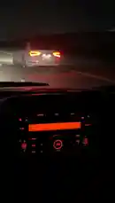 This first-person perspective footage captures a car driving on a dark road at night. The camera focuses on the illuminated orange dashboard and radio display, showing 'FM AM' and 'PWR'. Ahead, the bright red taillights of a white sedan are visible through the windshield, creating a moody and atmospheric scene. by @zf_v81 with Original Sound by zf_v81
