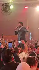 Experience the electrifying atmosphere of a Mohamed Fouad concert. The singer, dressed in a sharp suit, performs passionately on stage, surrounded by a massive, enthusiastic crowd. Fans hold up their phones to record the moment, creating a sea of screens under the vibrant red and orange stage lights. The energy is palpable as the audience sings along, fully immersed in the live music. by @mo.fouadziko with Original Sound by mo.fouadziko