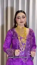 A woman, identified by on-screen text as WEDAD | وداد المنهالي, performs a graceful dance in front of a curtain. She is dressed in an ornate purple outfit with intricate patterns and wears multiple layers of elaborate gold necklaces and earrings. The accompanying Arabic music enhances the cultural and festive atmosphere of the performance. by @wedad_23g with Original Sound by wedad_23g